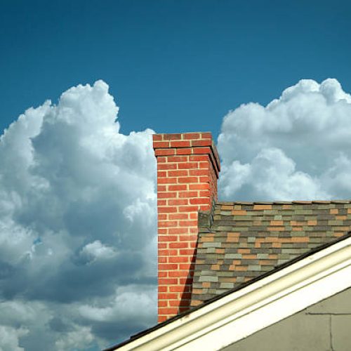 Part of tiled roof with brick chimney against blue sky with beautiful cloud formations and diagonal composition